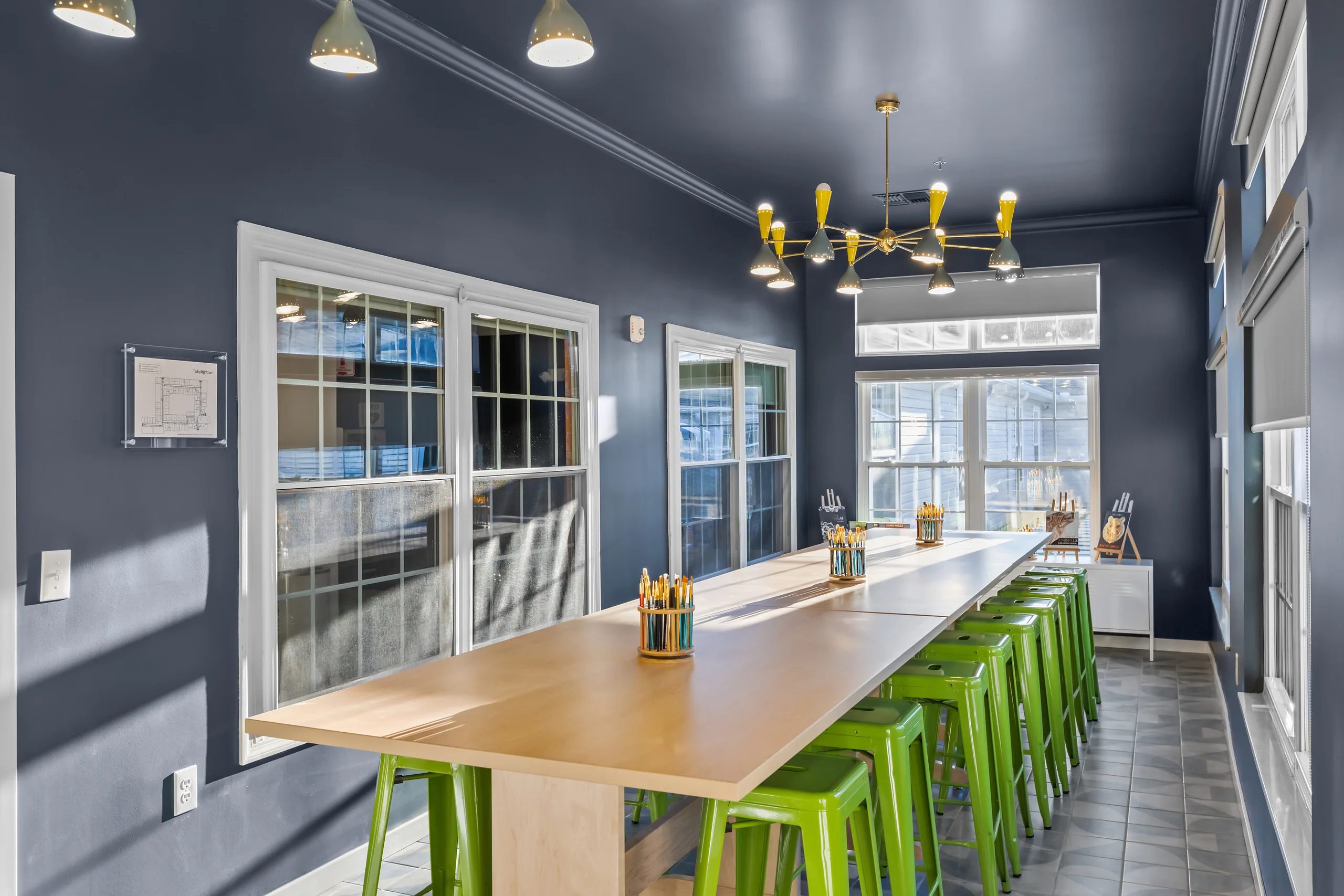 Modern dining area with a long wooden table and green stools under pendant lights.