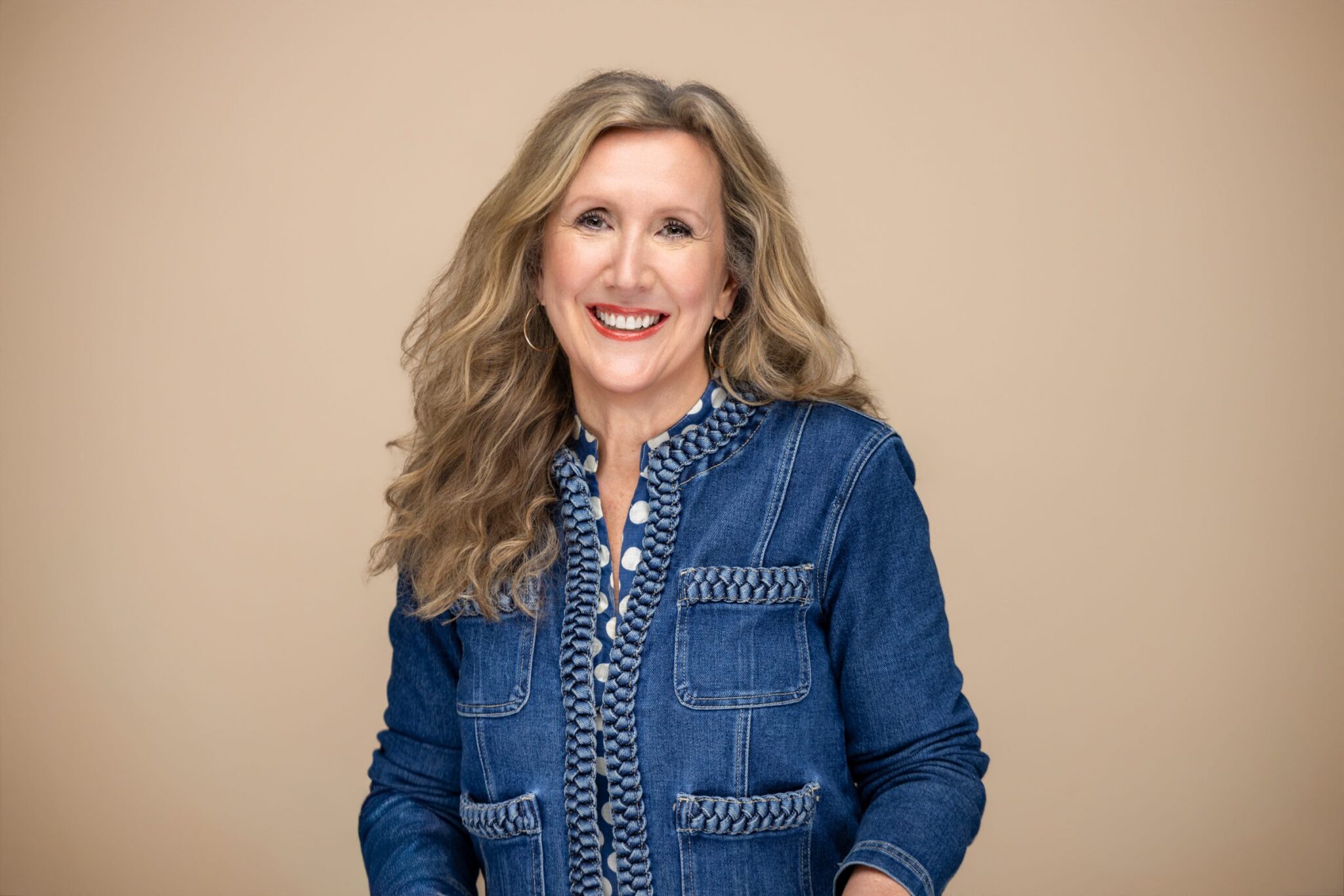 Smiling woman in a blue denim jacket against a beige background.