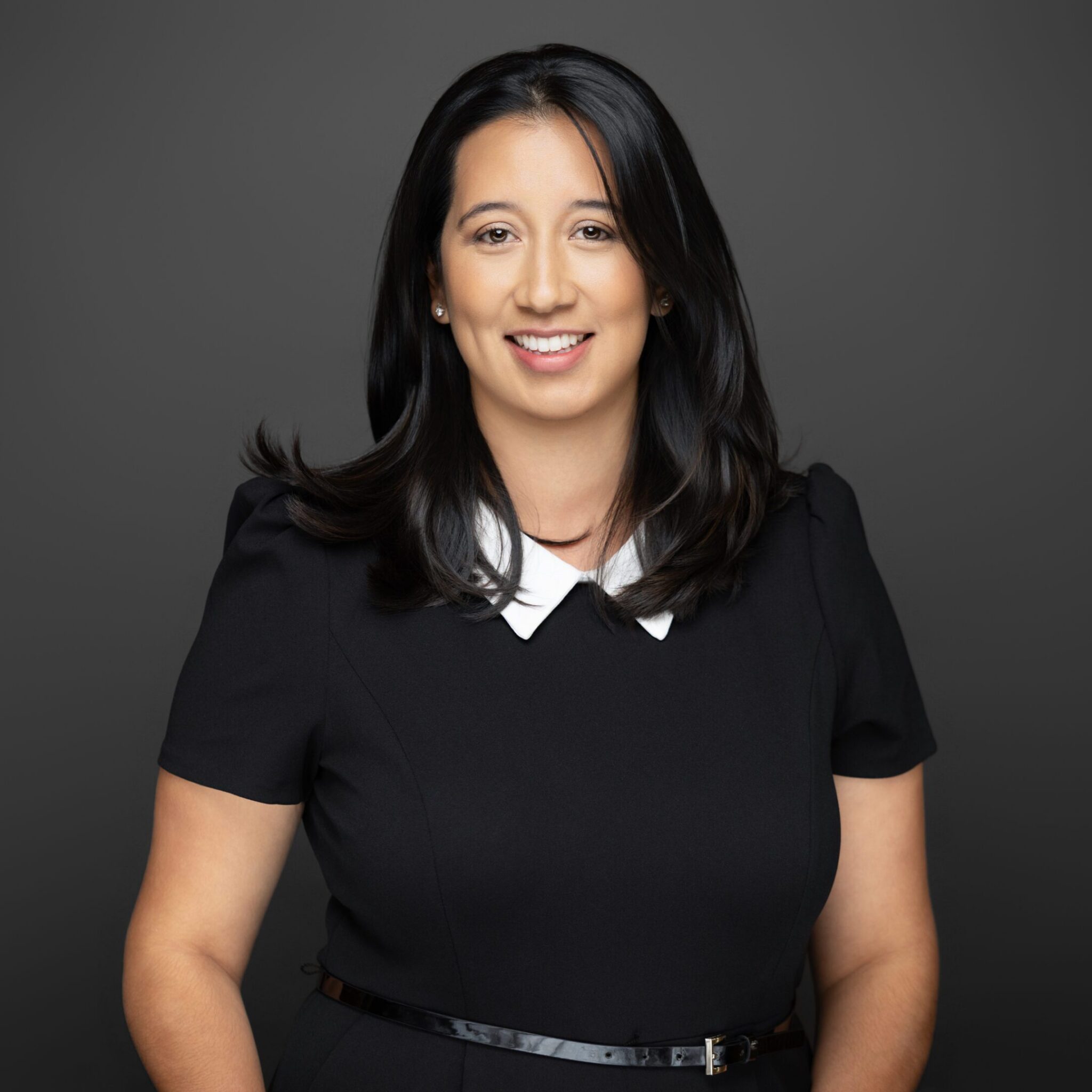 Professional woman with dark hair in a black dress with white collar.