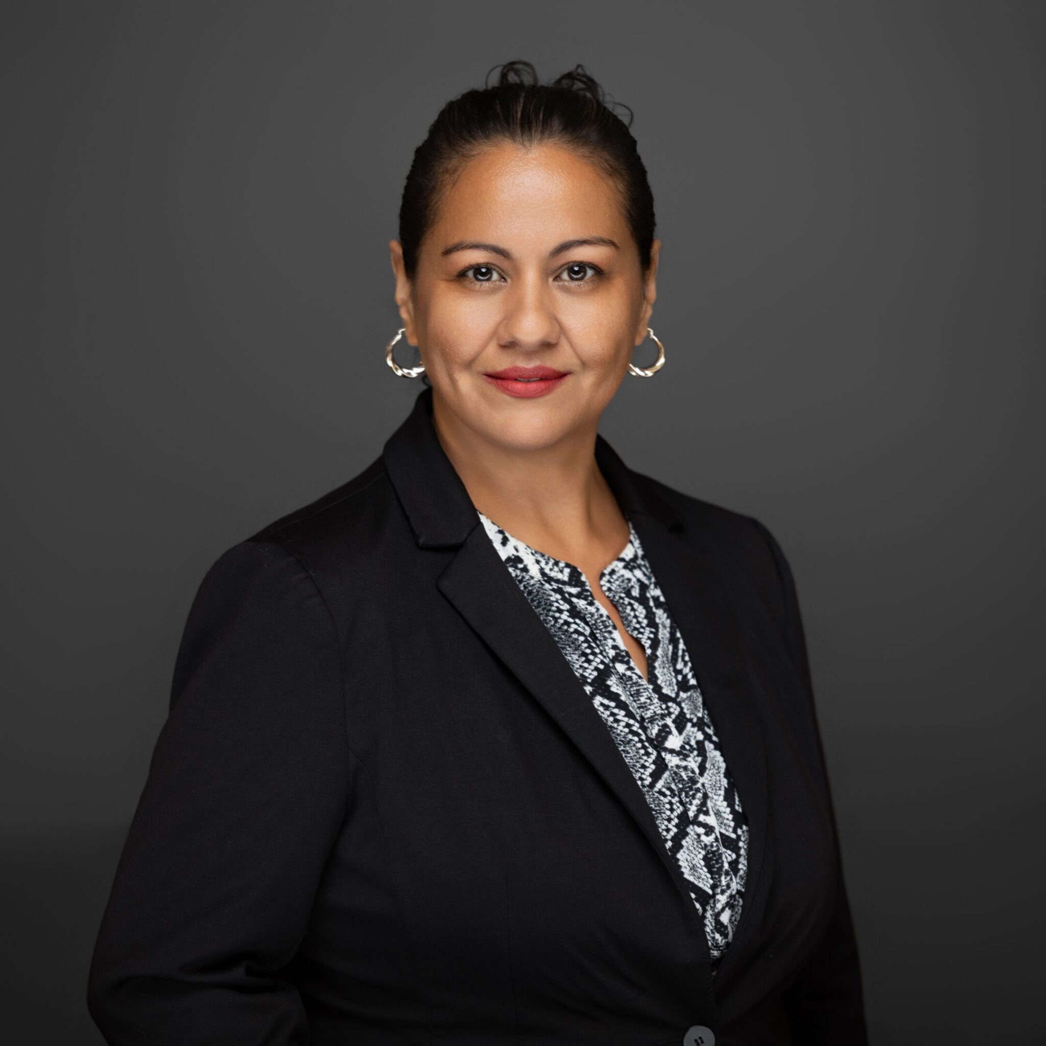 Professional woman in a black blazer posing against a gray backdrop.