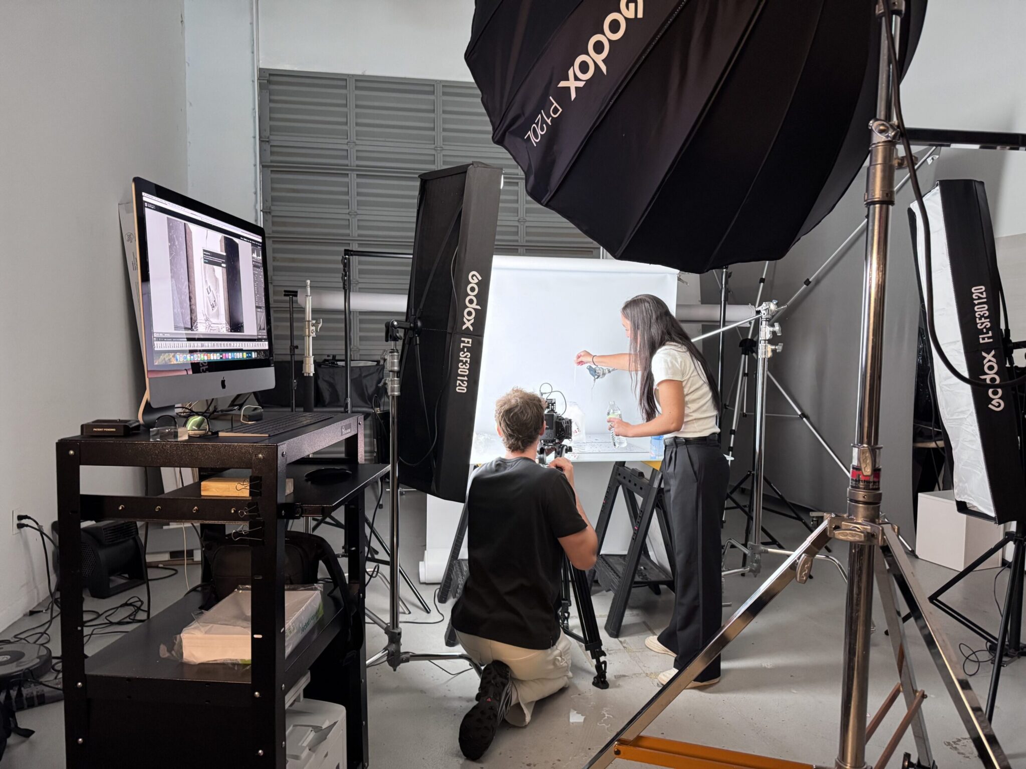 Photographer and assistant setting up a product shoot with lighting and computer monitors.