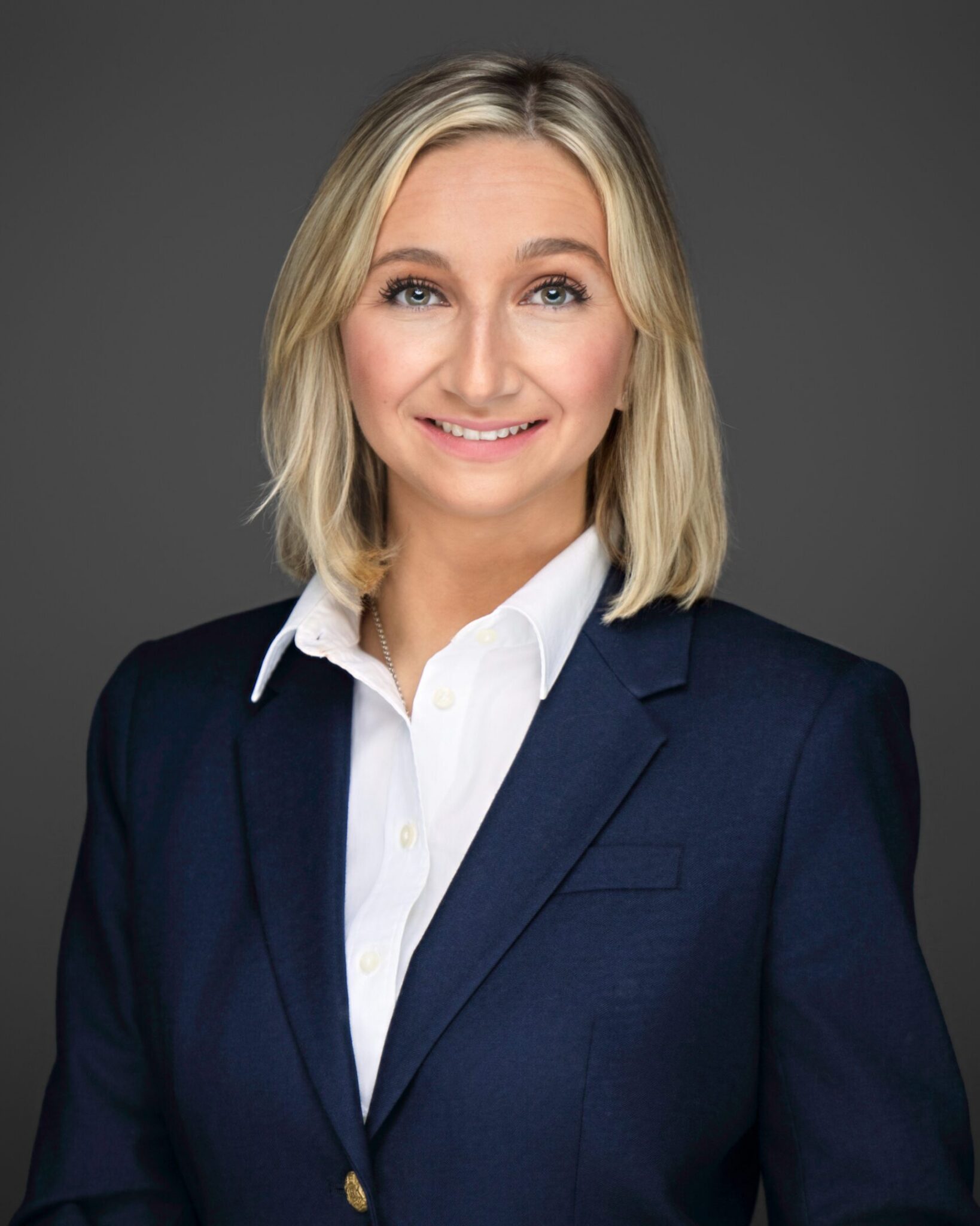 Professional woman in a navy blazer and white shirt against a gray background.